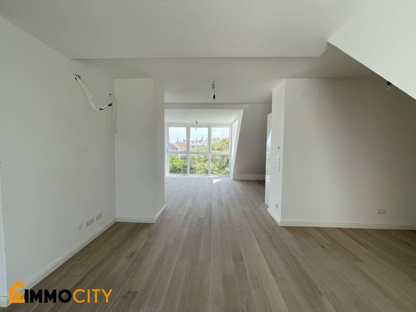 Geräumiges Zimmer mit Holzboden, weißen Wänden und viel Tageslicht durch die Fenster.