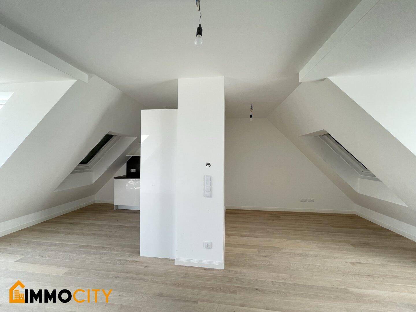 Offener Wohnbereich mit Holzboden, Dachschrägen und Blick auf die moderne Küchenzeile.