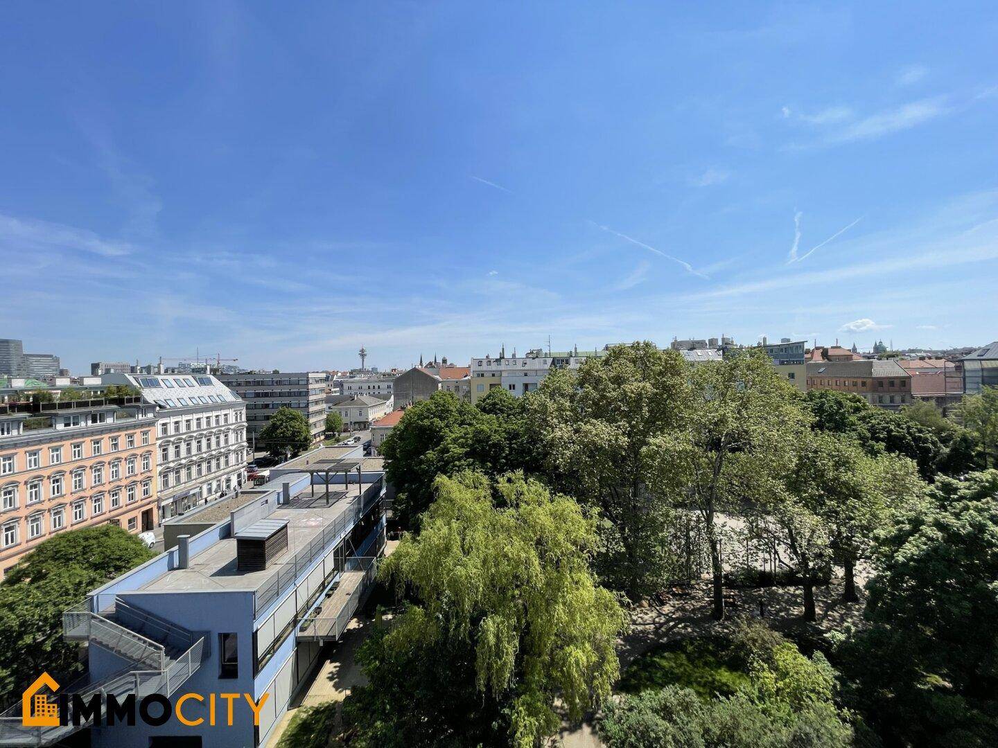 Panoramablick über die Stadt mit grünen Bäumen und historischen Gebäuden unter blauem Himmel.