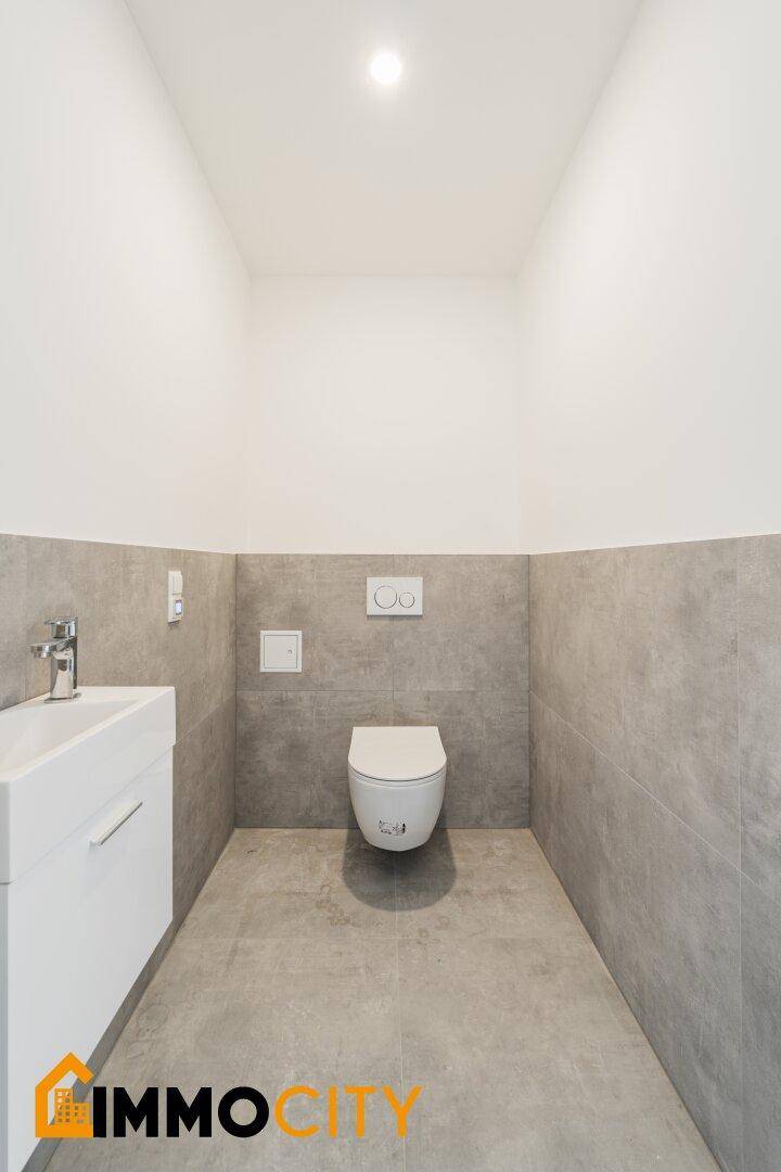 Helles Gäste-WC mit modernen Armaturen und grauen Wand- und Bodenfliesen.