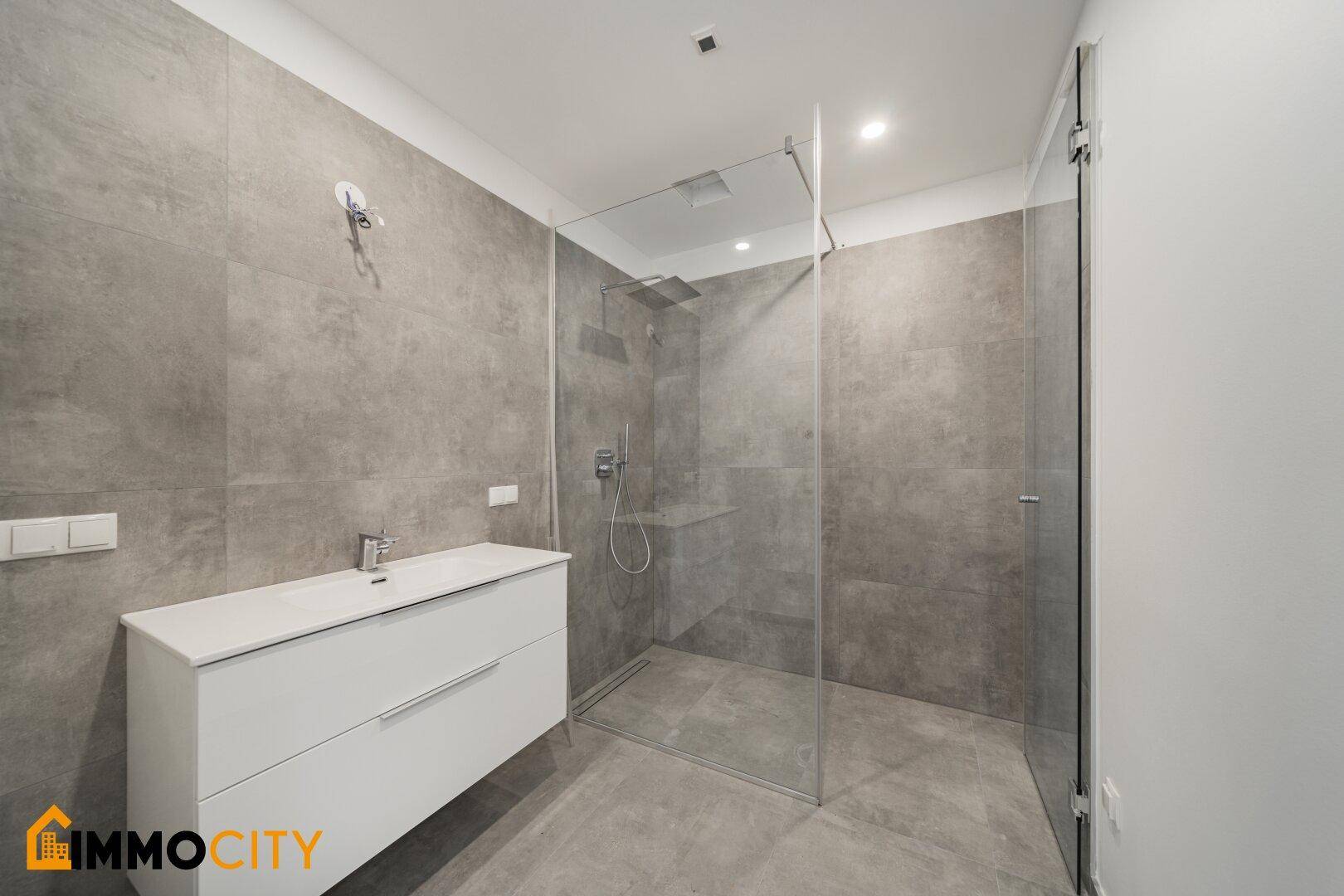 Modernes Badezimmer mit großer begehbarer Dusche und grauem Fliesenboden.