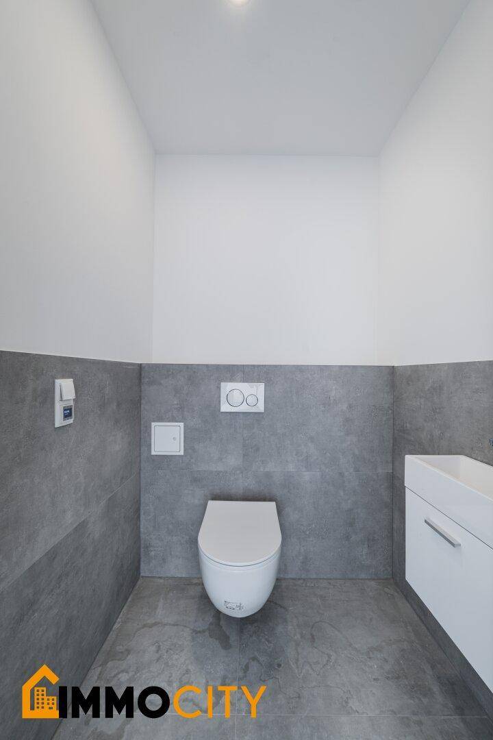 Modernes Gäste-WC mit Wand-WC, kleinem Waschbecken und grauen Fliesen.