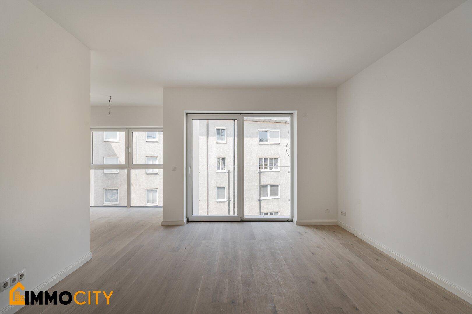 Geräumiger, heller Wohnbereich mit Holzboden und Zugang zu einem Balkon oder einer Terrasse.