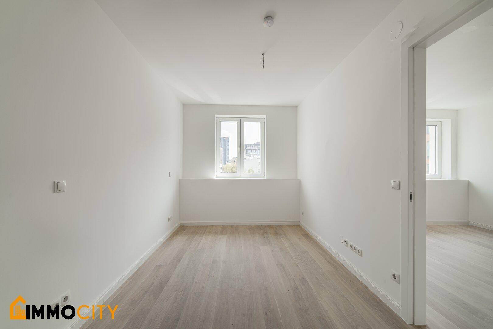 Leeres Zimmer mit großen Fenstern und hellem Parkettboden, ideal als Schlaf- oder Arbeitszimmer.
