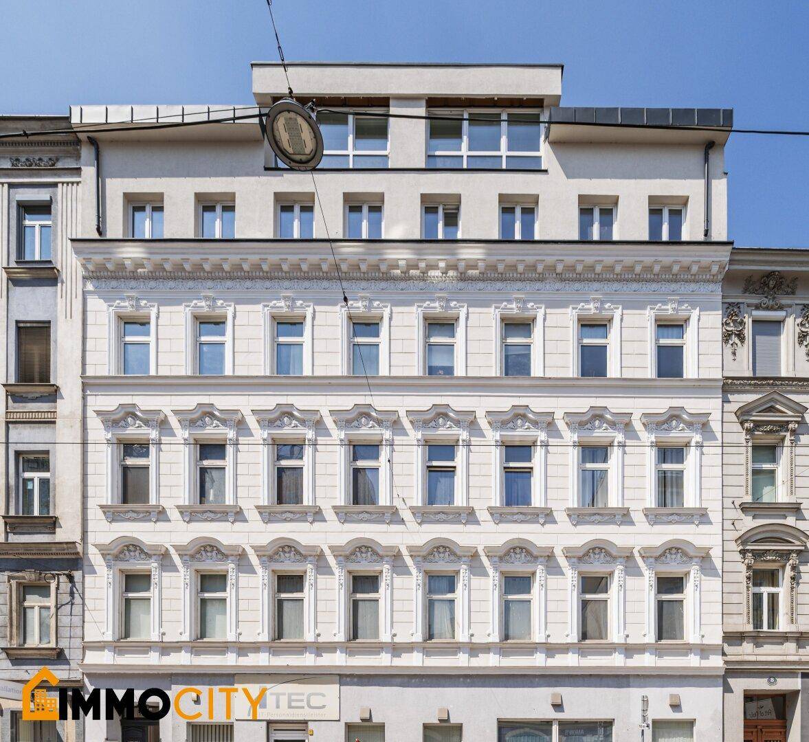 Historische Fassade eines Altbaus mit aufgesetztem modernen Dachgeschoss in städtischer Umgebung.