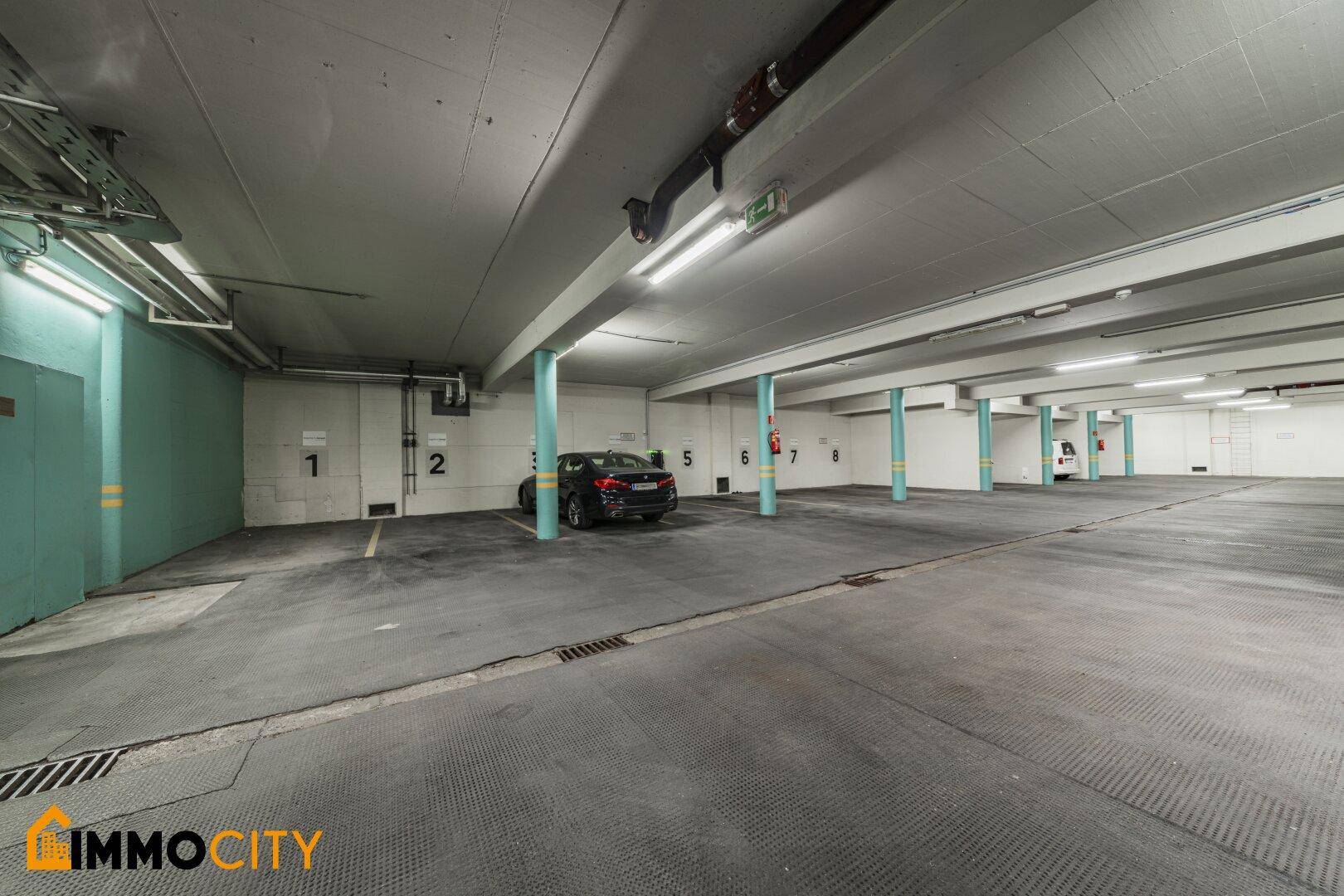 Geräumige und gut beleuchtete Tiefgarage mit nummerierten Stellplätzen und Betonboden.