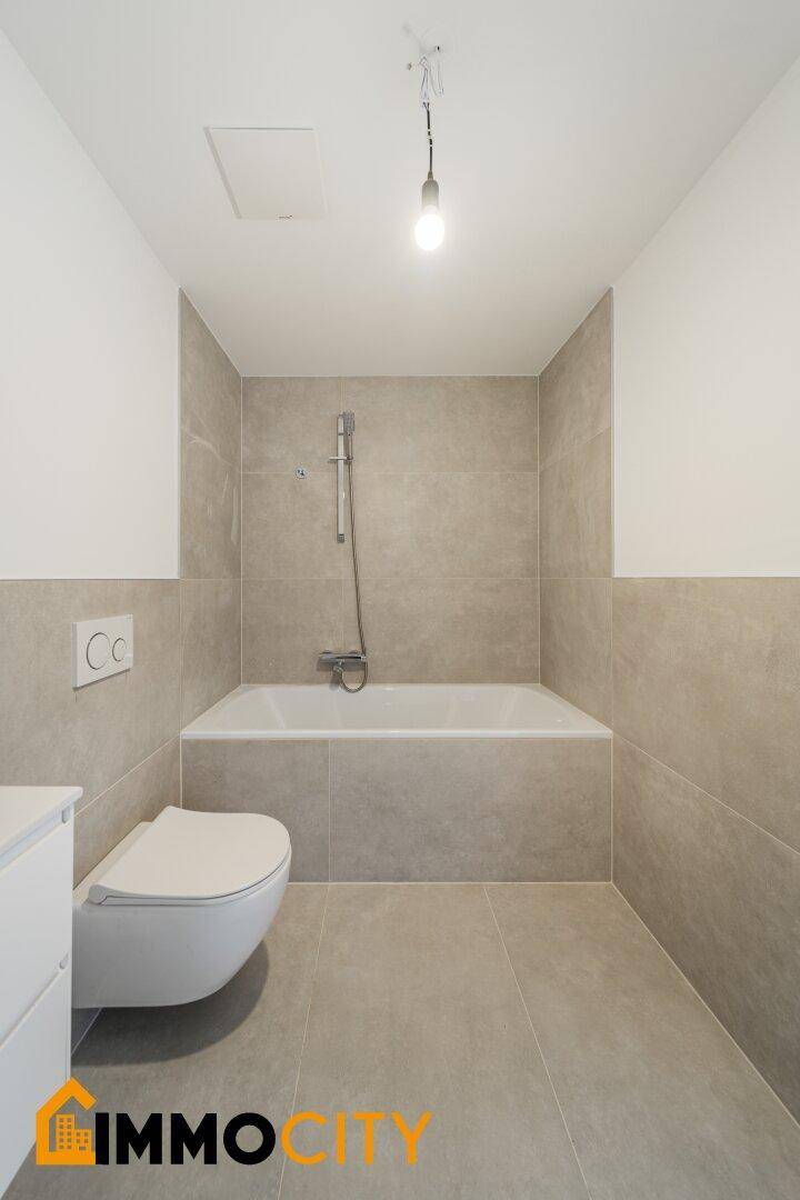 Modernes Badezimmer mit Badewanne, Wand-WC und grauen Fliesen.