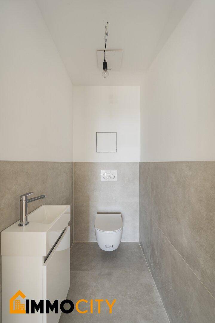 Modernes Gäste-WC mit Wand-WC, kleinem Waschbecken und grauen Fliesen.