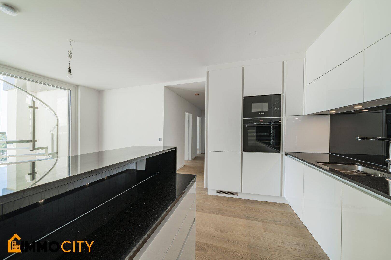 Moderne Küche mit integriertem Backofen, schwarzen Arbeitsplatten und Holzparkett.