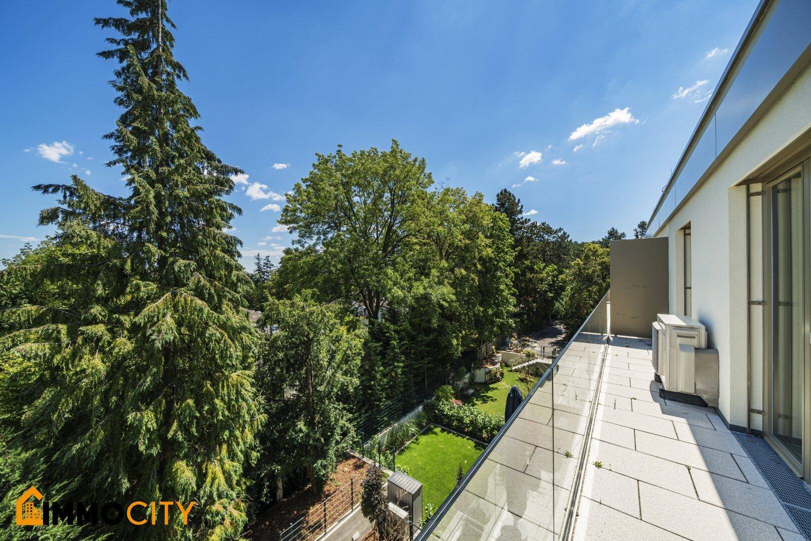 Langer Balkon mit Glasgeländer und Blick auf den gepflegten Garten.