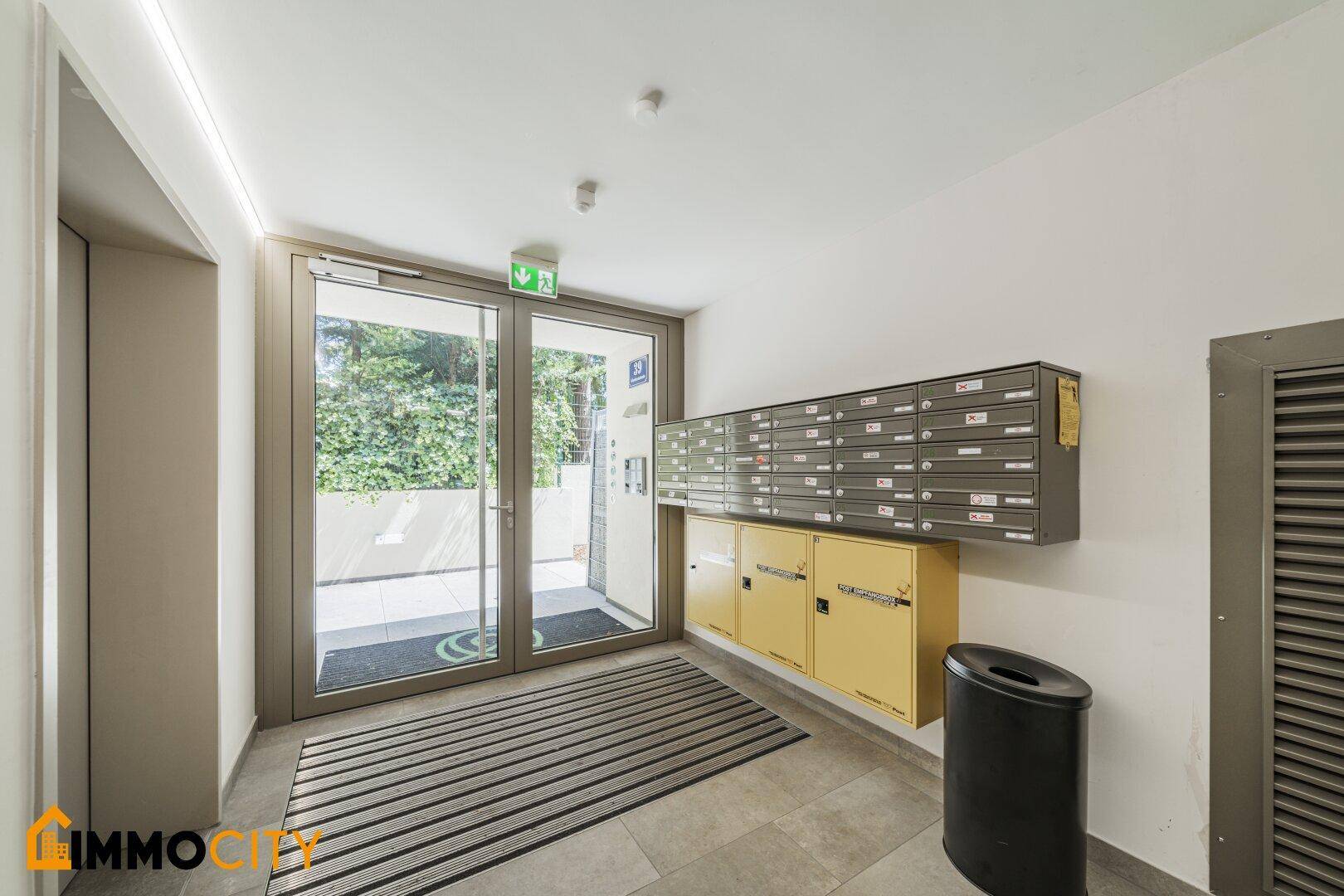 Eingangsbereich mit Briefkästen, großen Glastüren und Blick ins Grüne.