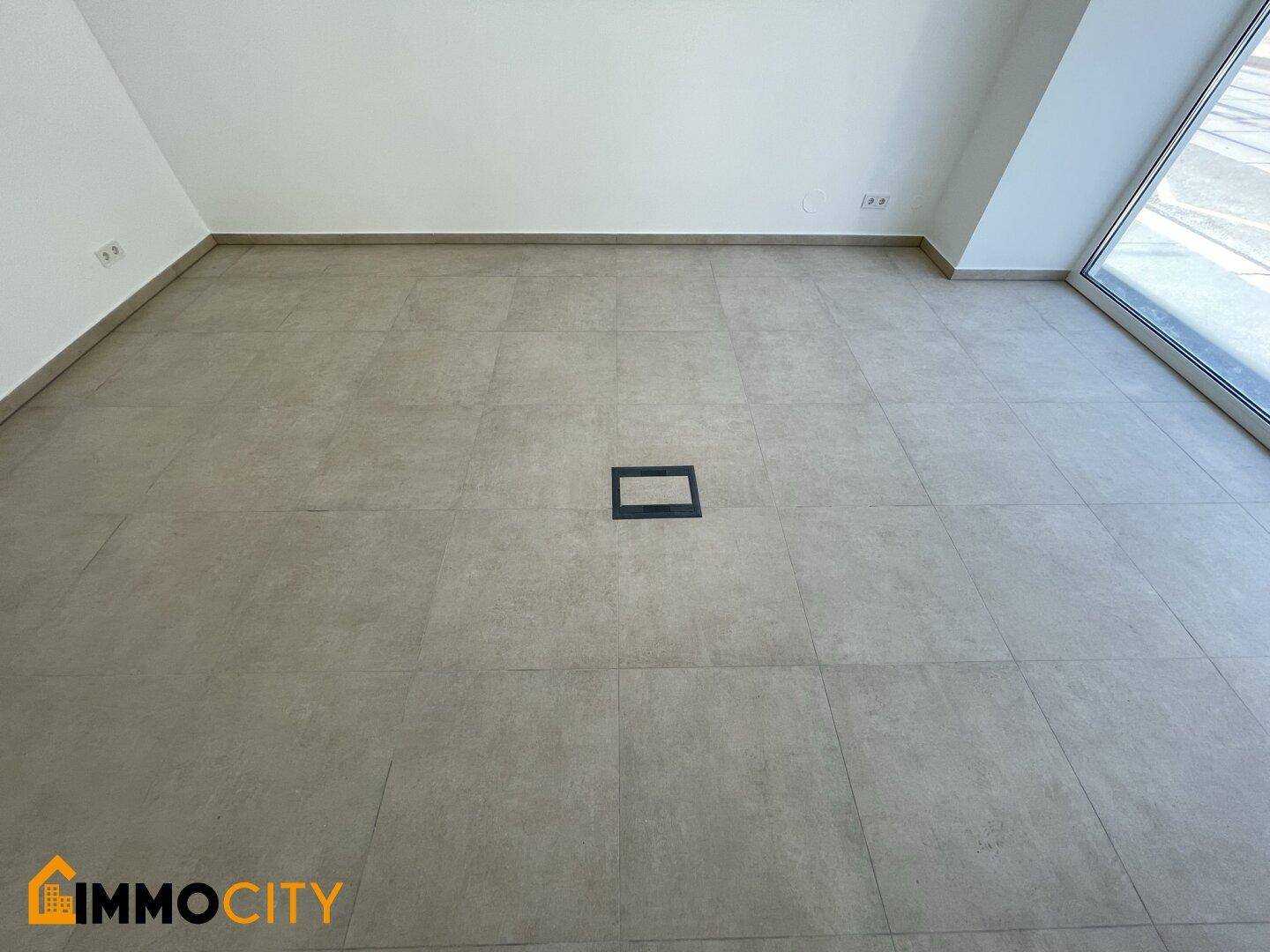 Detailaufnahme des modernen Fliesenbodens mit einer Bodensteckdose in der Mitte des Raumes.