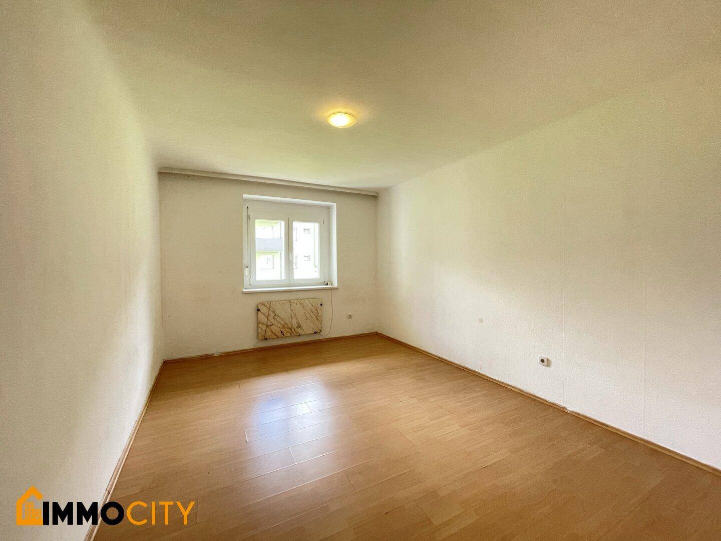 Helles Schlafzimmer mit Laminatboden und Fenster, bereit zur individuellen Gestaltung.