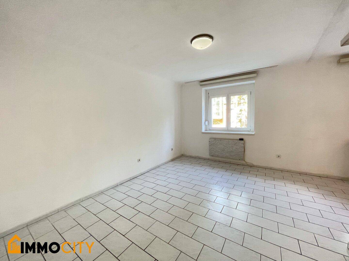 Heller Wohnbereich mit Fliesenboden und Fenster, bietet viel Gestaltungspotenzial.