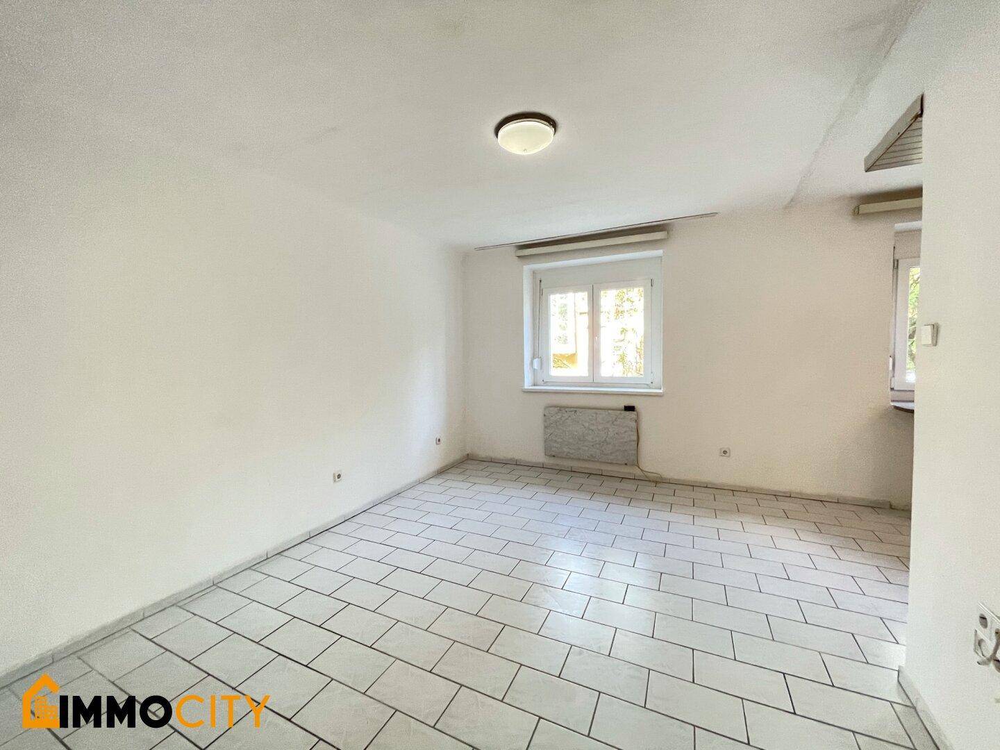 Geräumiger Wohnbereich mit Fliesenboden und Fenster, ideal für gemütliche Stunden.