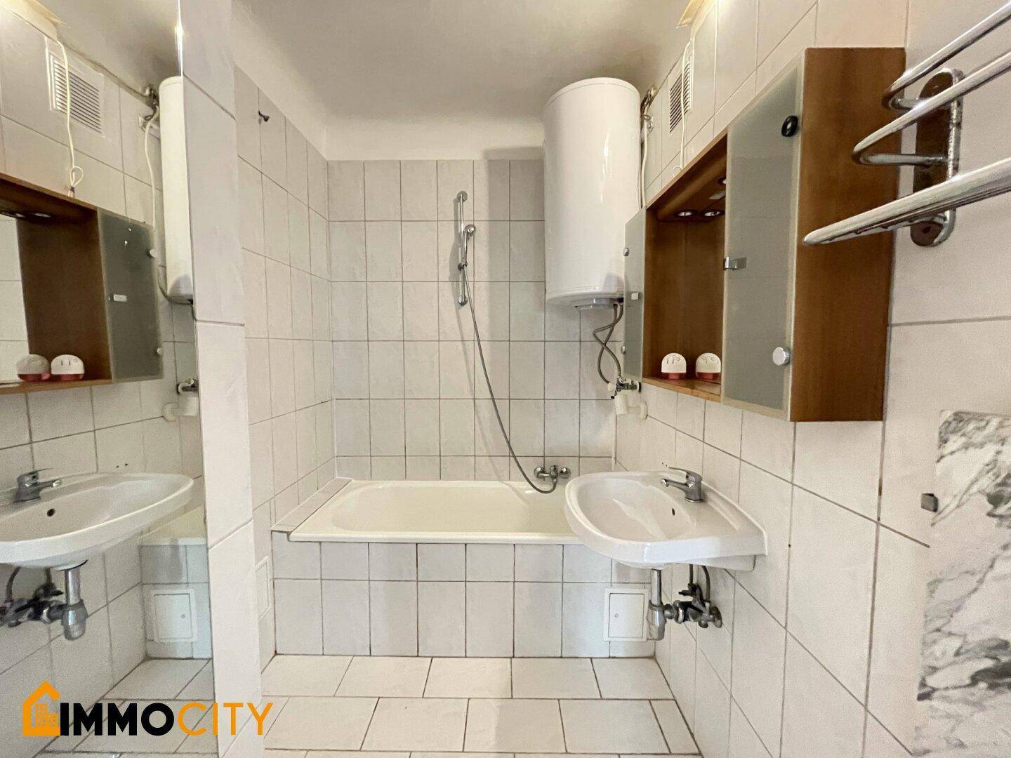 Funktionales Badezimmer mit Badewanne, Waschbecken und Boiler, komplett gefliest.