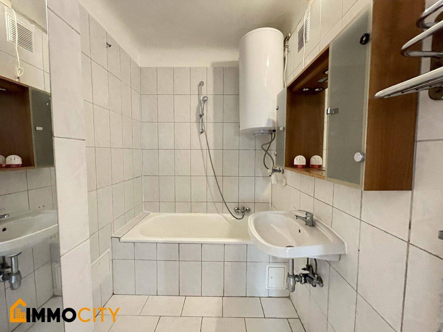Einfaches Badezimmer mit Badewanne, Waschbecken und Boiler, vollständig gefliest.