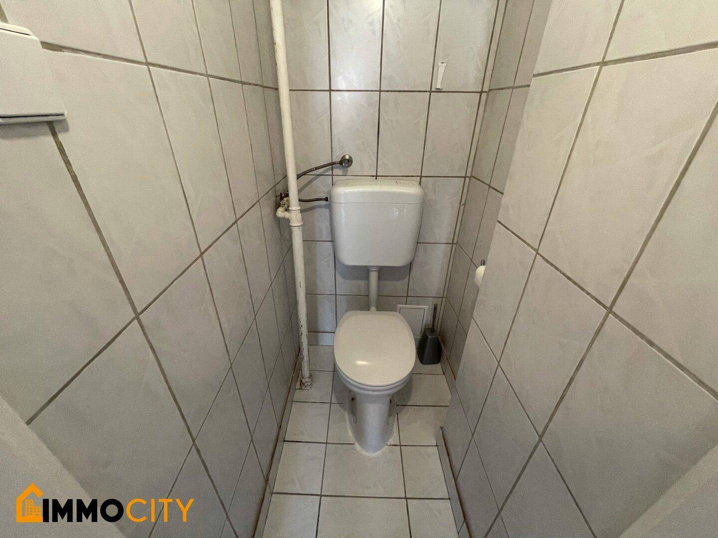 Separates WC mit Fliesenboden und Standard-Toilette.
