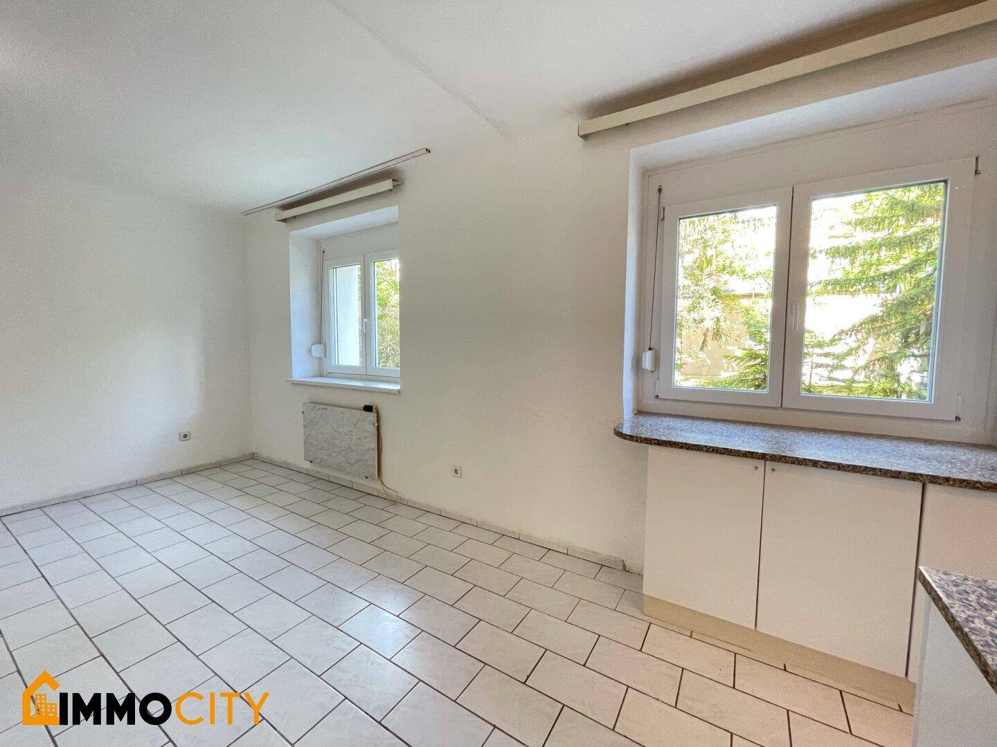 Geräumiger Wohnbereich mit Fliesenboden und Blick ins Grüne durch die Fenster.