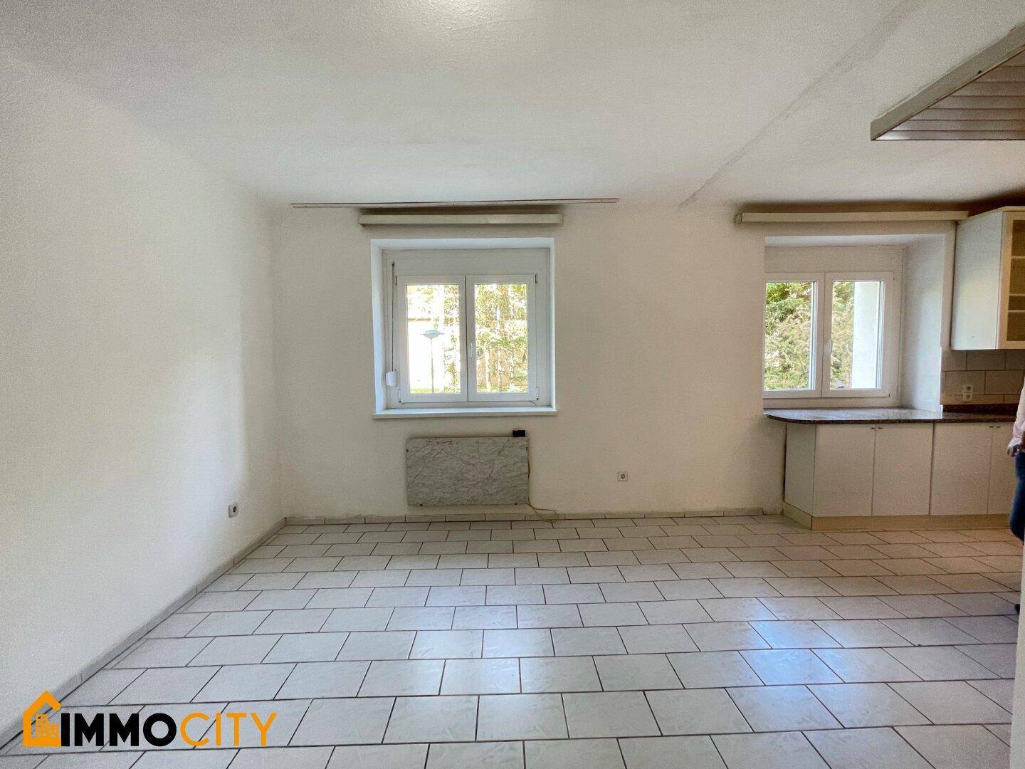 Heller Wohnbereich mit Fliesenboden und integrierter Küchenzeile, bietet viel Licht.