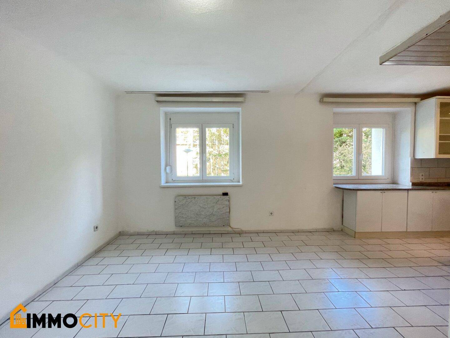 Geräumiger Wohnbereich mit Fliesenboden und Fenster, ideal für individuelle Einrichtung.