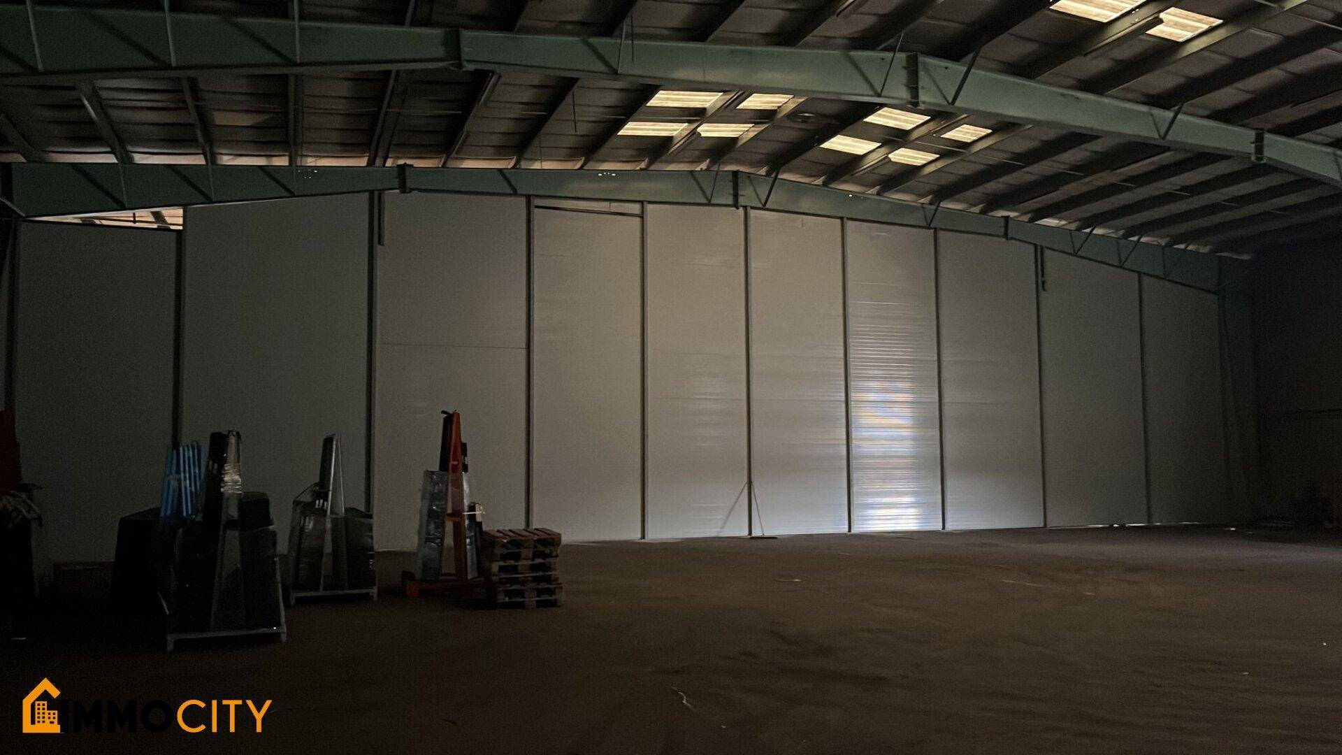 Geräumige Lagerhalle mit hoher Decke, sichtbaren Metallträgern und Oberlichtern für natürliches Licht.