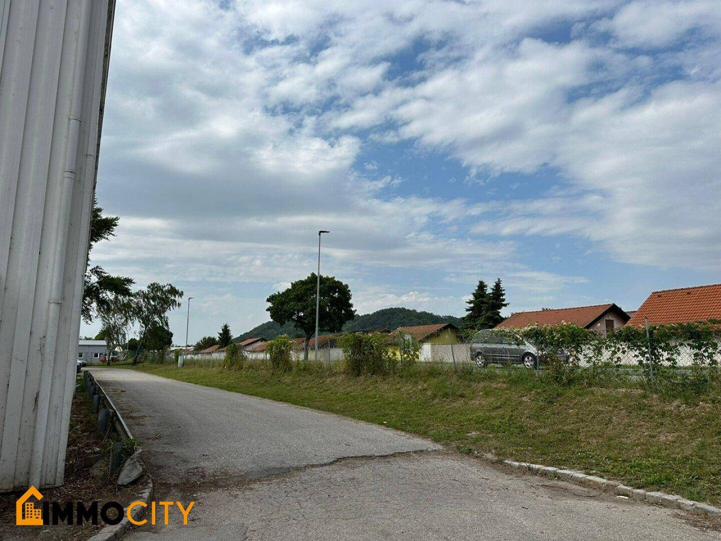 Straße neben dem Industriegebiet mit Blick auf Wohnhäuser und grüne Hügel in der Ferne.