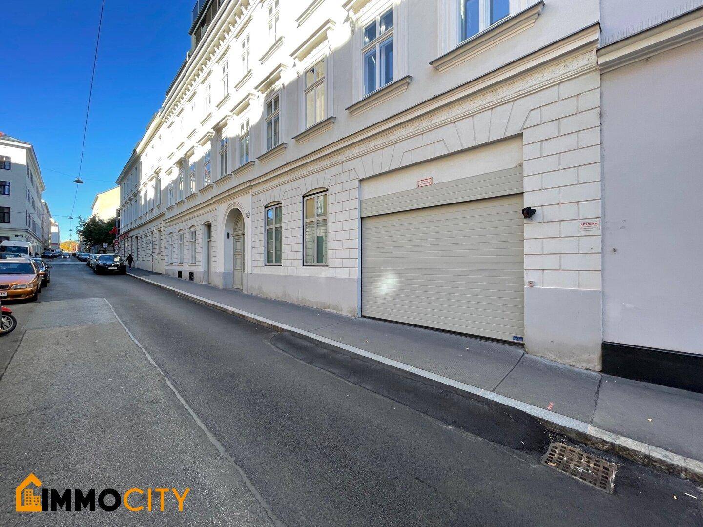 Lange Fassade eines historischen Gebäudes mit integrierter Garageneinfahrt entlang einer ruhigen Straße.