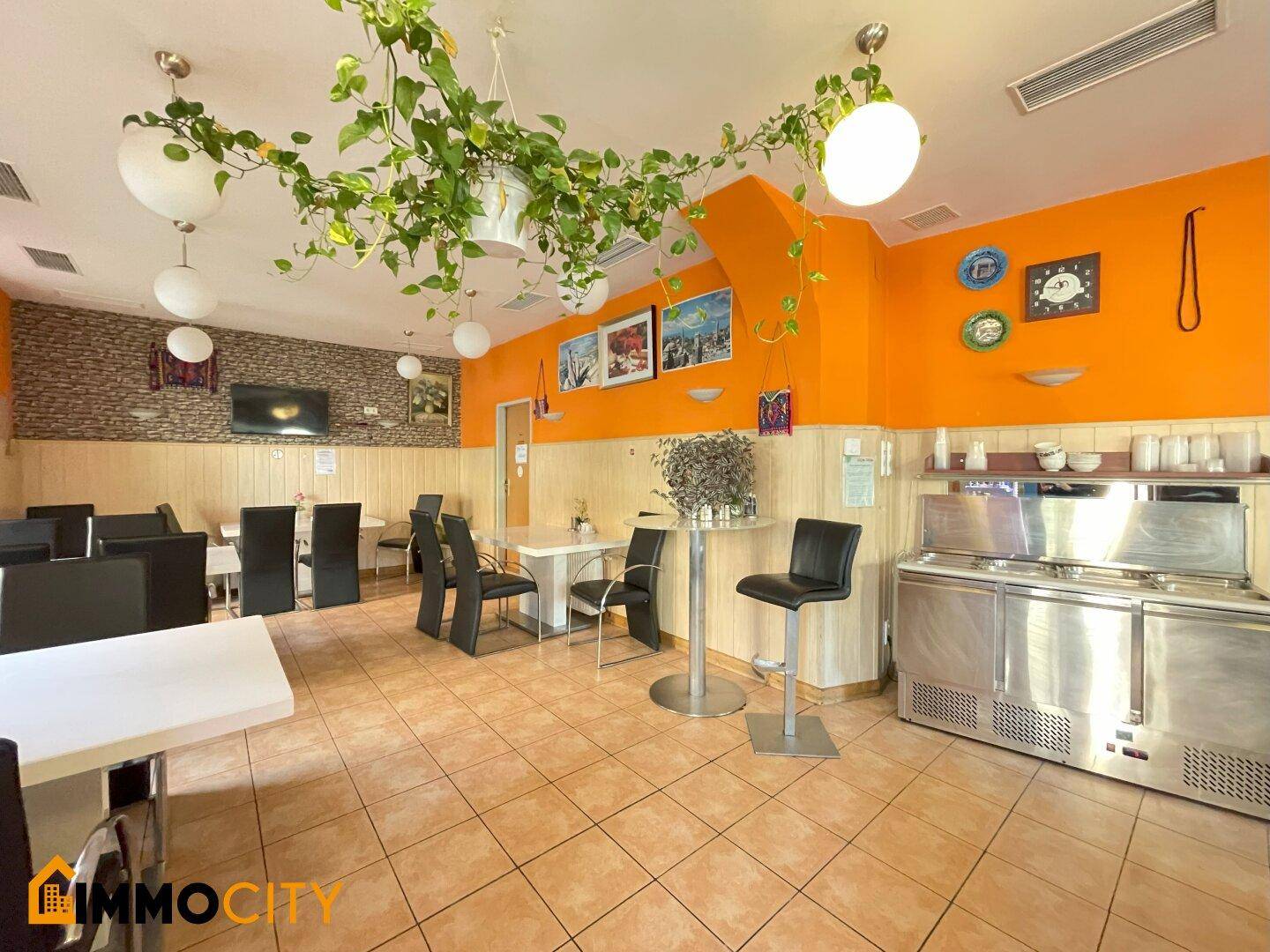 Heller Restaurantbereich mit gefliestem Boden, orangefarbenen Wänden und einer Theke mit Kühlgeräten.