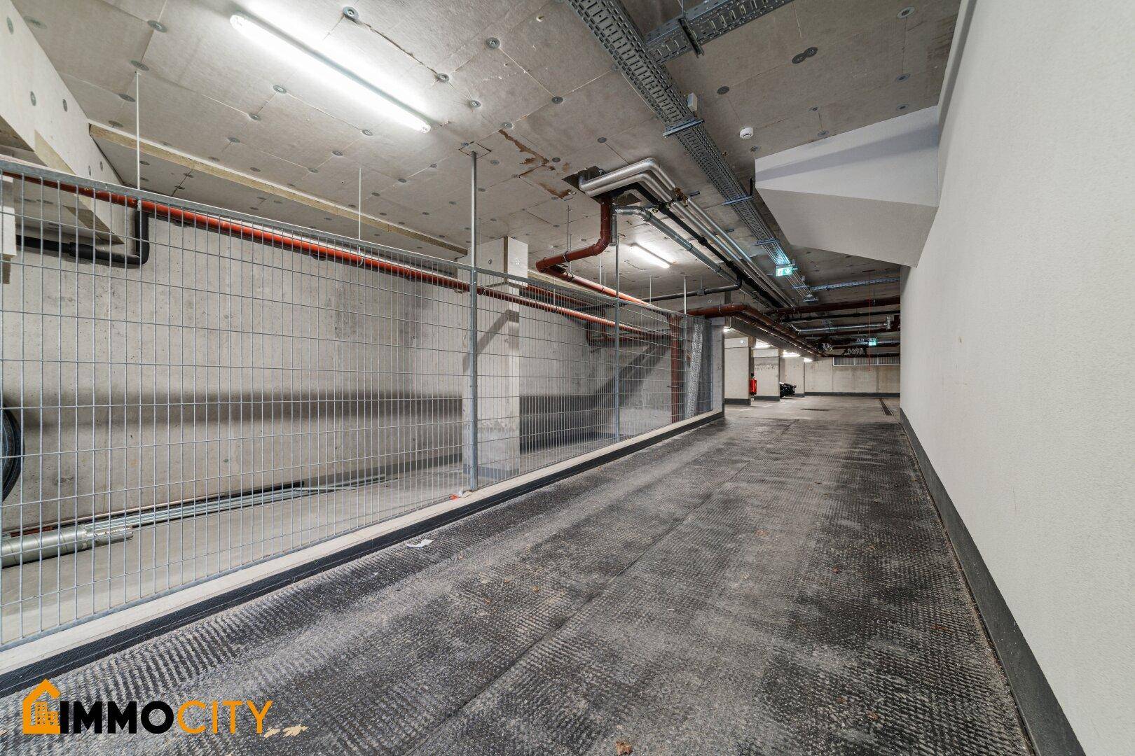 Zufahrt zur Tiefgarage mit Gitterabtrennung und sichtbaren Rohren an der Decke.