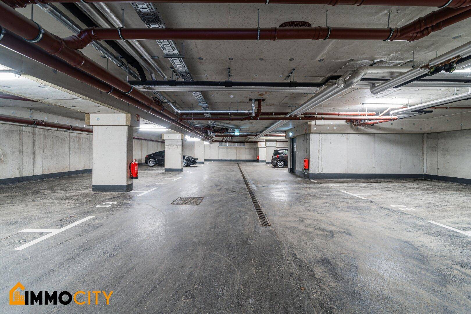 Tiefgarage mit markierten Stellplätzen und sichtbaren Versorgungsleitungen an der Decke.