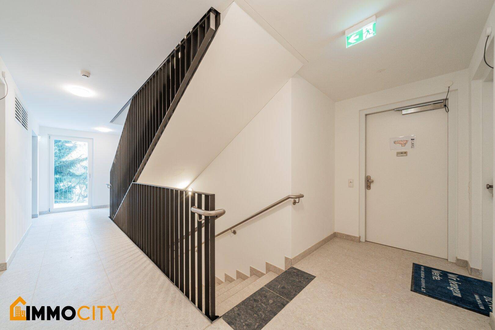 Modernes Treppenhaus mit dunklem Geländer und hellem Fliesenboden.