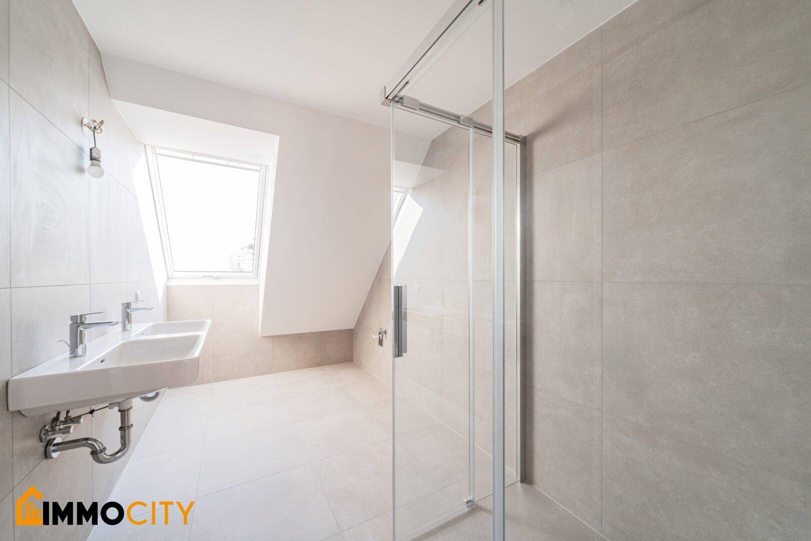 Modernes Badezimmer mit grauen Fliesen, Doppelwaschbecken und einer geräumigen begehbaren Dusche.