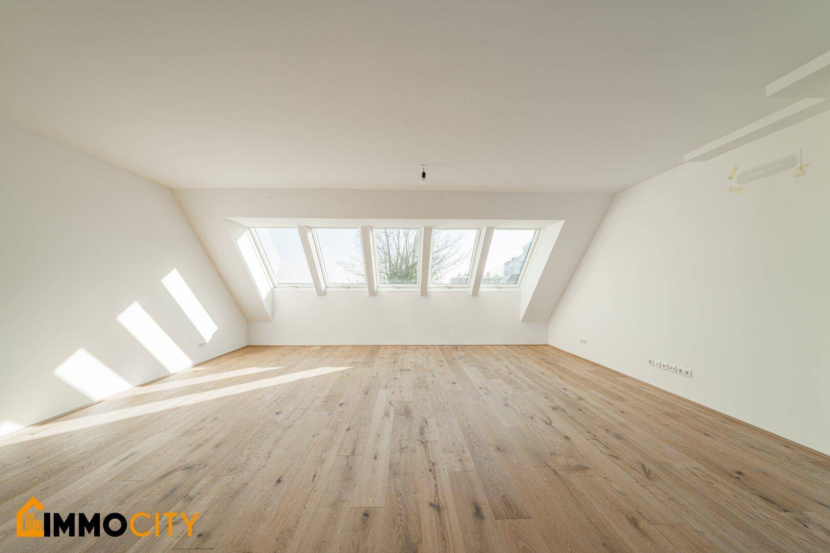 Helles Dachgeschosszimmer mit Holzboden und mehreren Dachfenstern, ideal für Wohn- oder Schlafbereich.