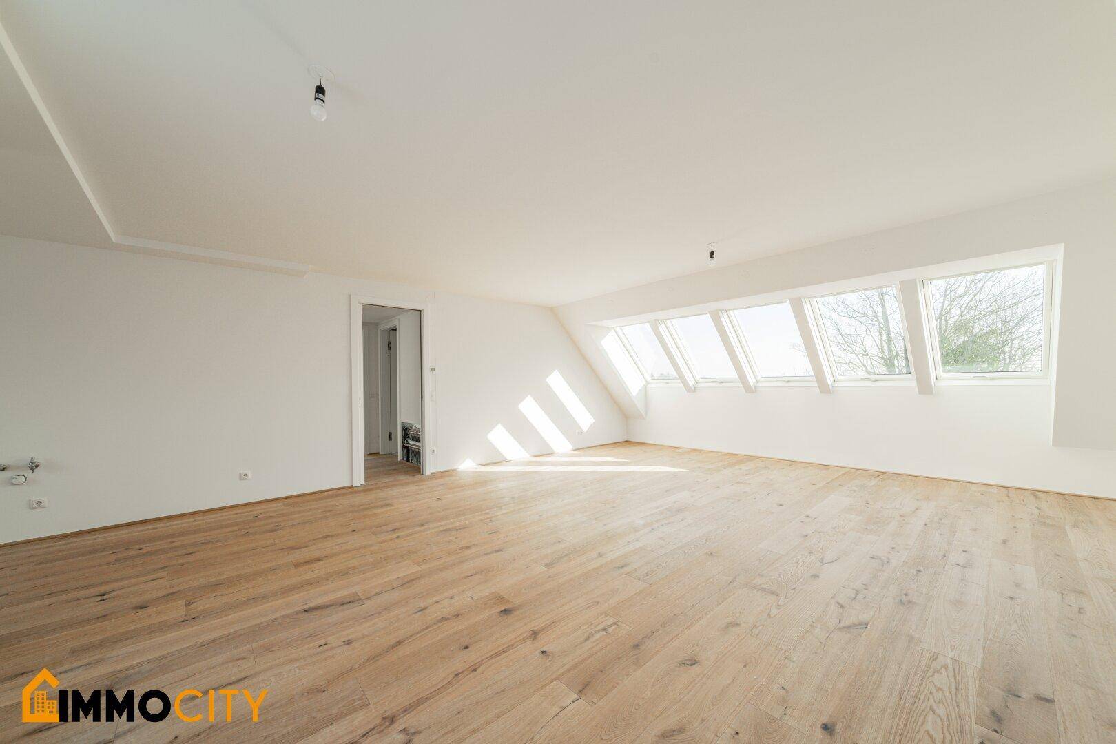 Helles Dachgeschosszimmer mit Holzboden und mehreren Dachfenstern, das viel Tageslicht hereinlässt.