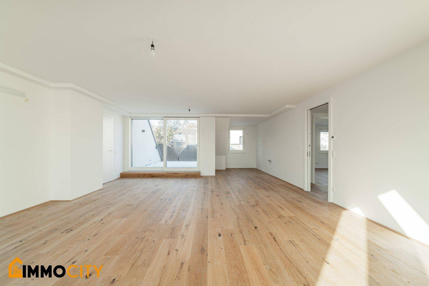 Geräumiges, helles Zimmer mit Holzboden und großer Schiebetür, die Zugang zum Außenbereich bietet.