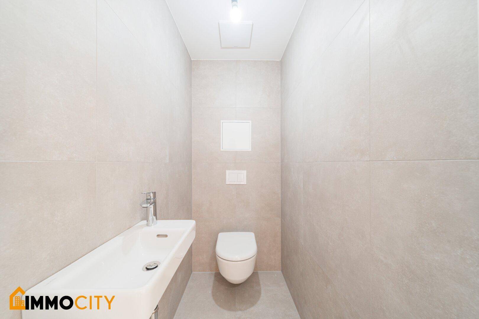 Modernes Gäste-WC mit wandmontierter Toilette, kleinem Waschbecken und hellgrauen Fliesen.