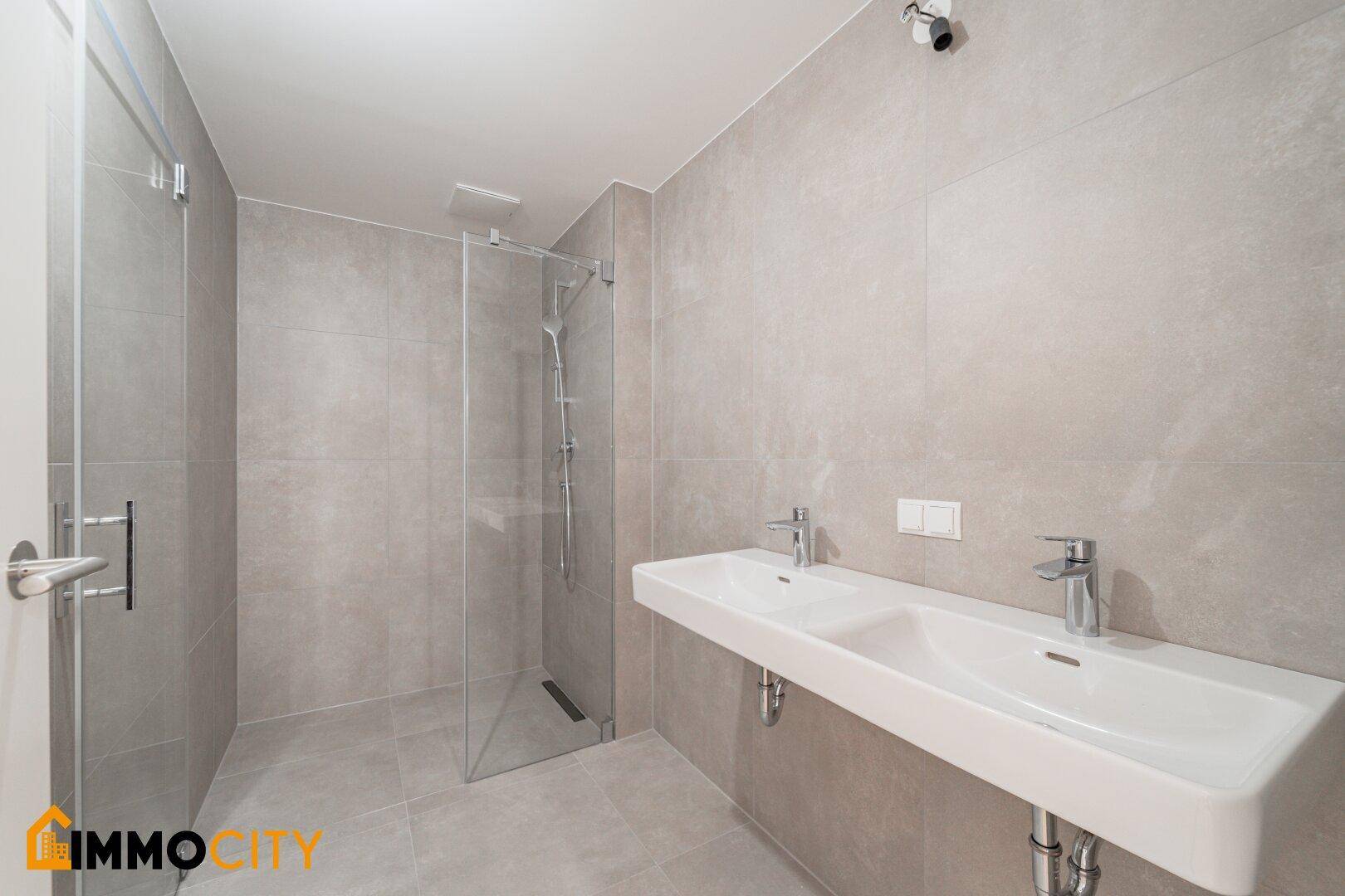 Modernes Badezimmer mit doppelten Waschbecken, großer begehbarer Dusche und grauen Fliesen.