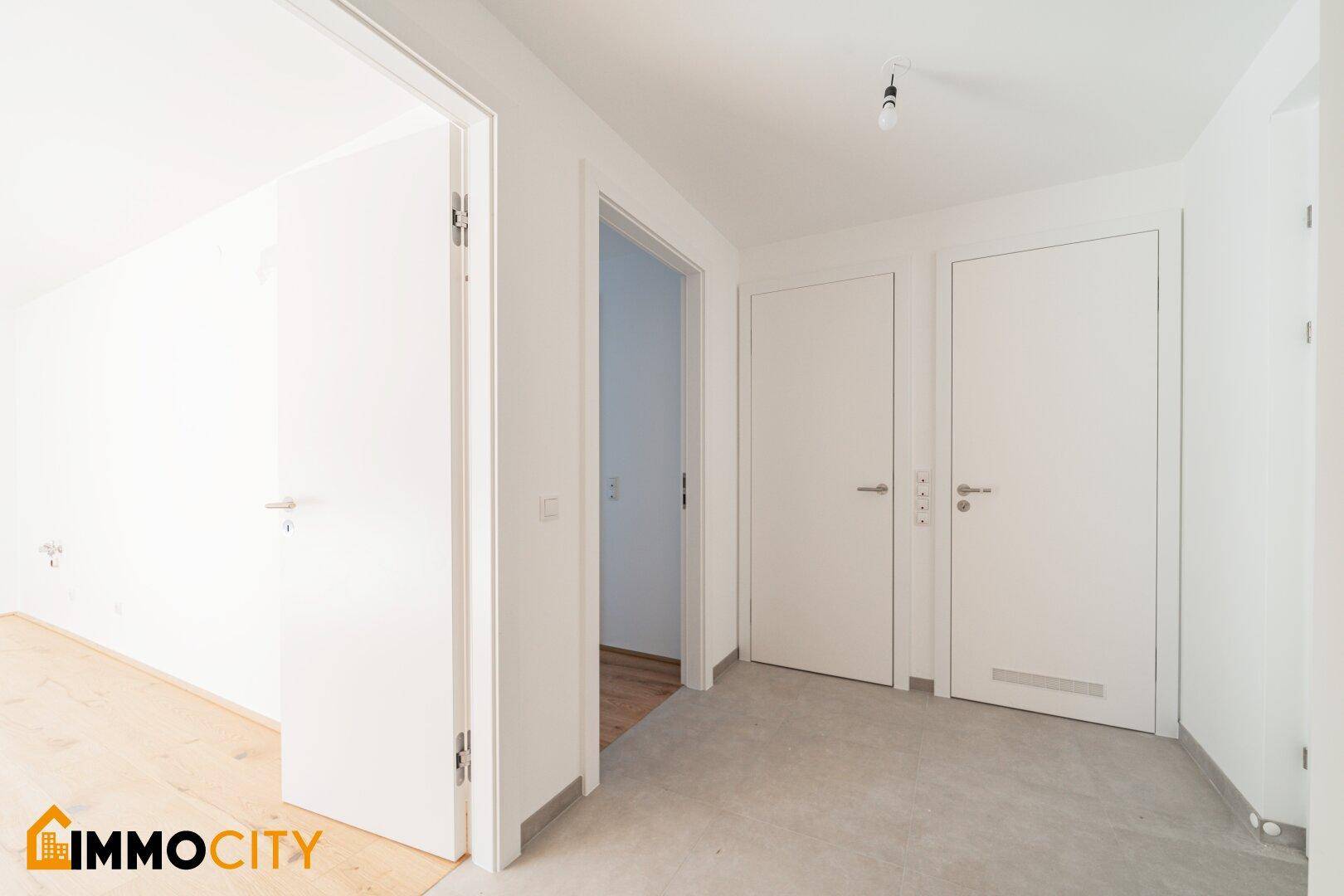 Heller Flur mit mehreren weißen Türen und einem Übergang zu einem Zimmer mit Holzboden.