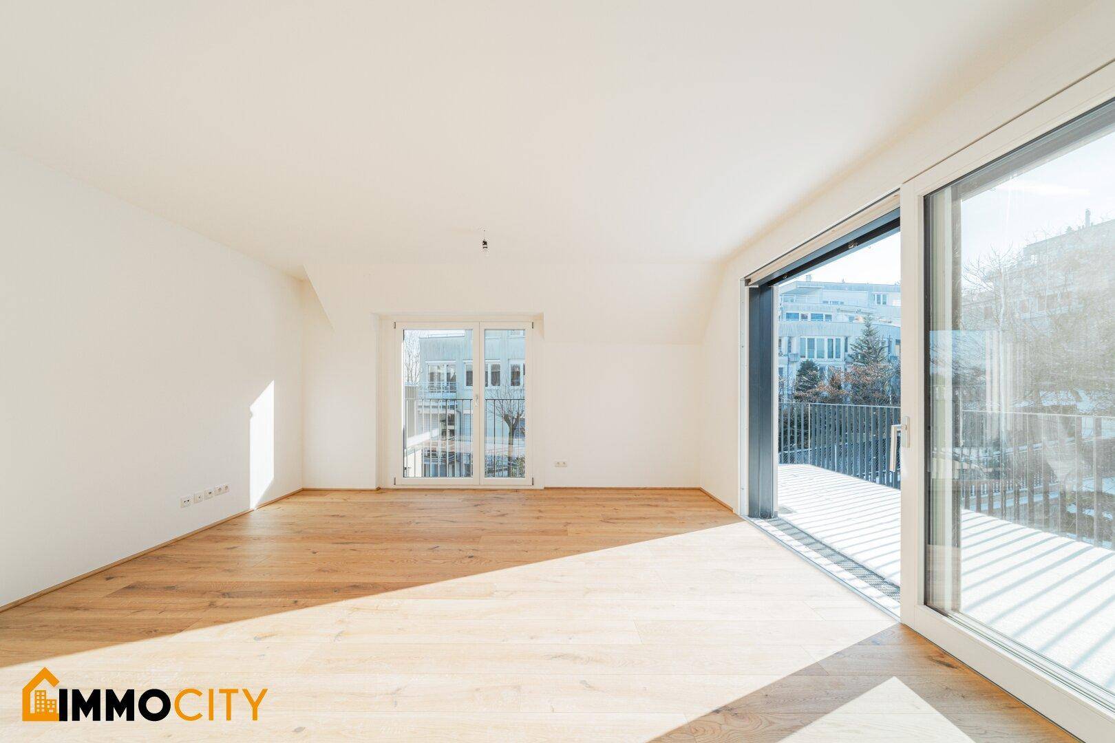 Geräumiges, helles Zimmer mit Holzboden und Zugang zu einem Balkon mit Blick auf die Umgebung.