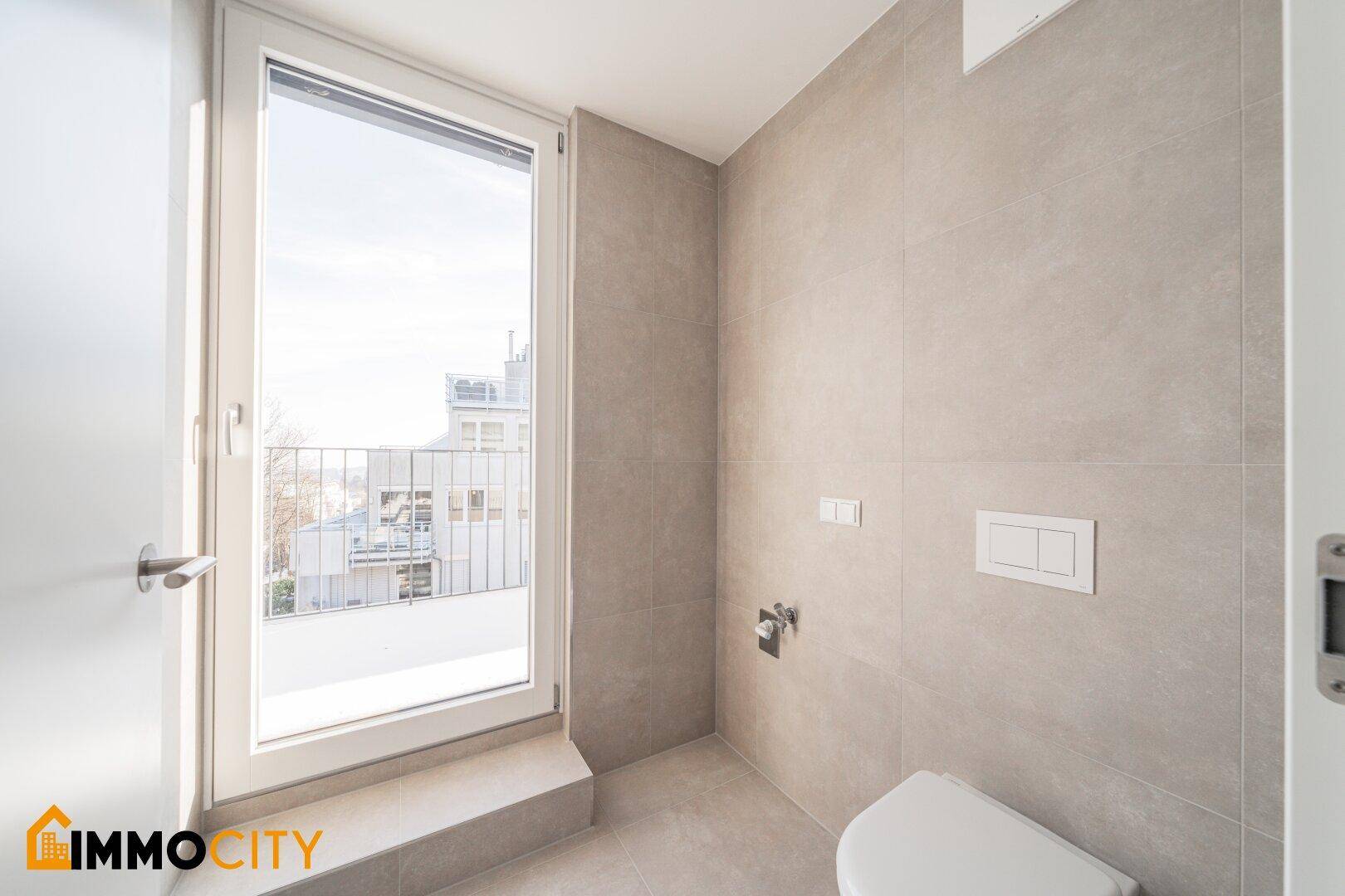 Modernes WC mit Fliesenboden, wandhängender Toilette und Fenster mit Balkonzugang.