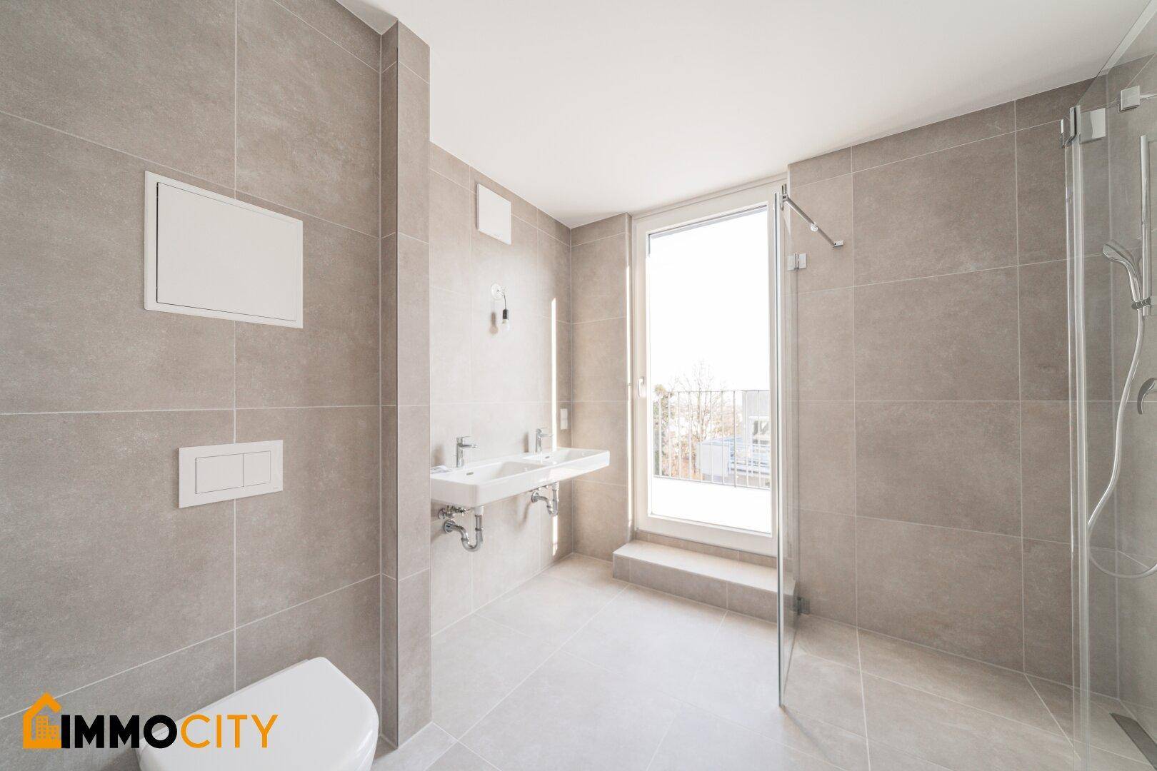 Modernes Badezimmer mit Fliesen, Toilette, Doppelwaschbecken und Balkonzugang.