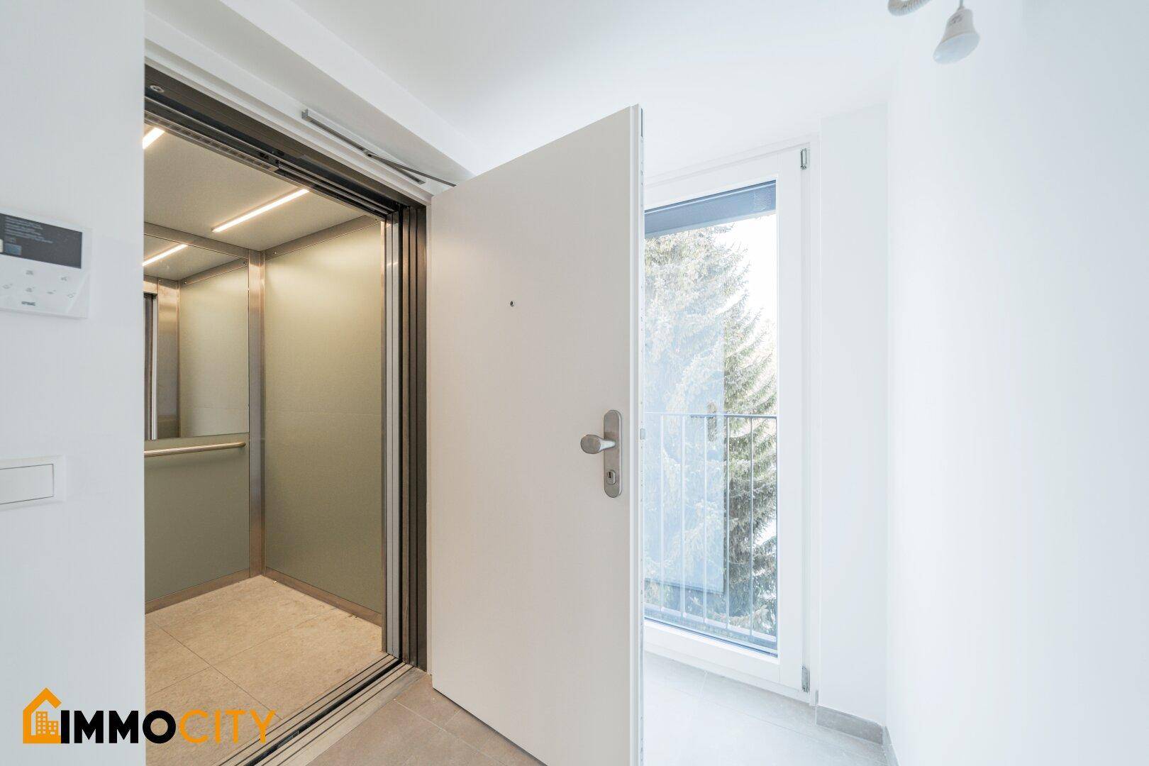 Eingangsbereich mit offenem Aufzug und Zugang zu einem kleinen Balkon.