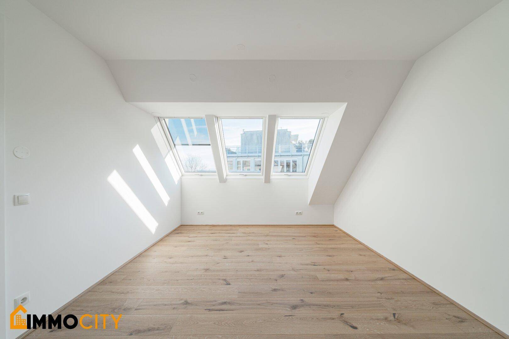 Helles Zimmer mit Holzboden und drei Dachfenstern, die viel Licht hereinlassen.
