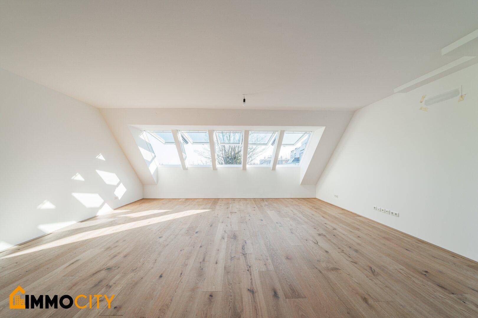 Heller Dachgeschossraum mit Holzboden und mehreren Dachfenstern, bietet viel natürliches Licht.