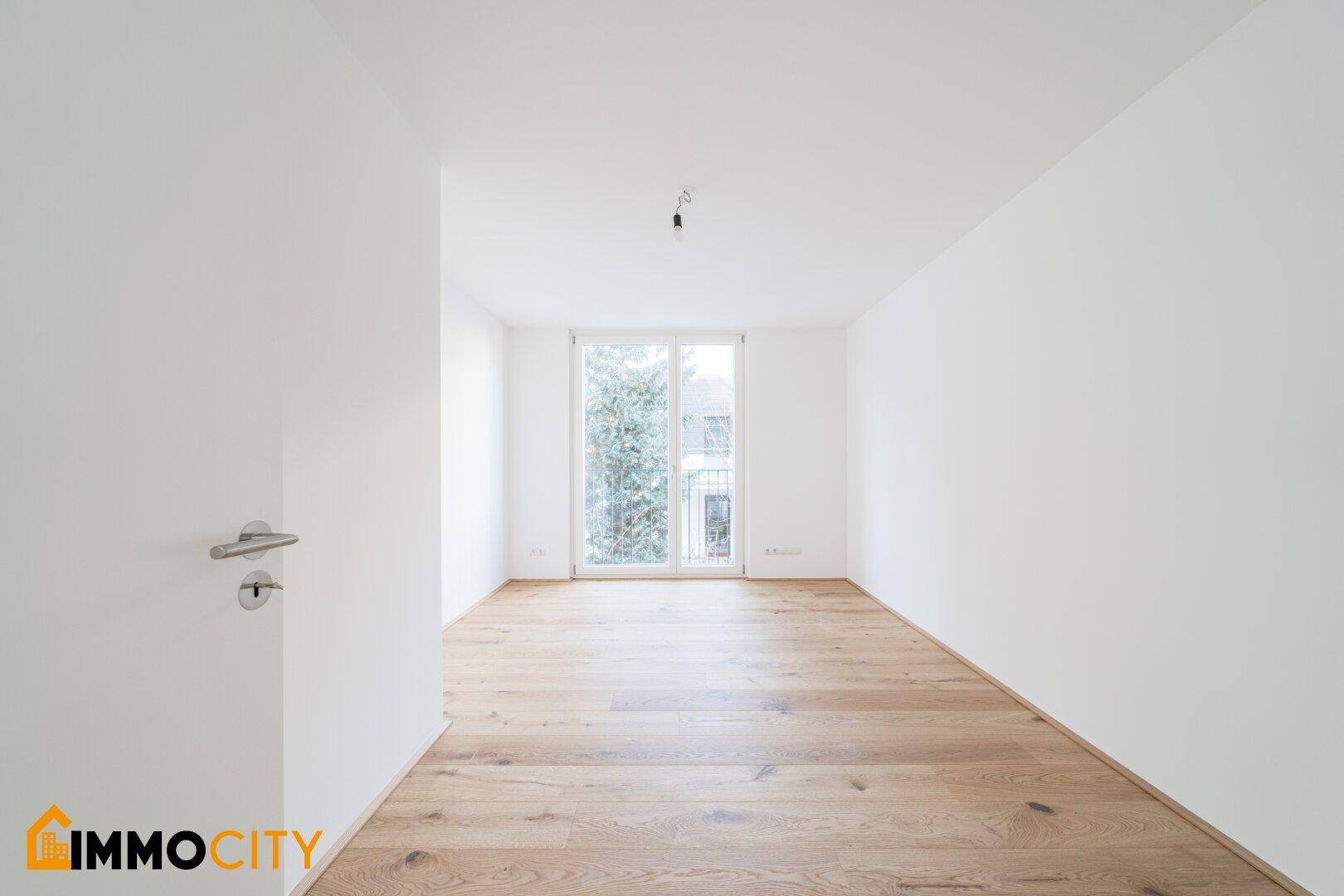 Helles Schlafzimmer mit Holzboden und Zugang zu einem französischen Balkon, unmöbliert.