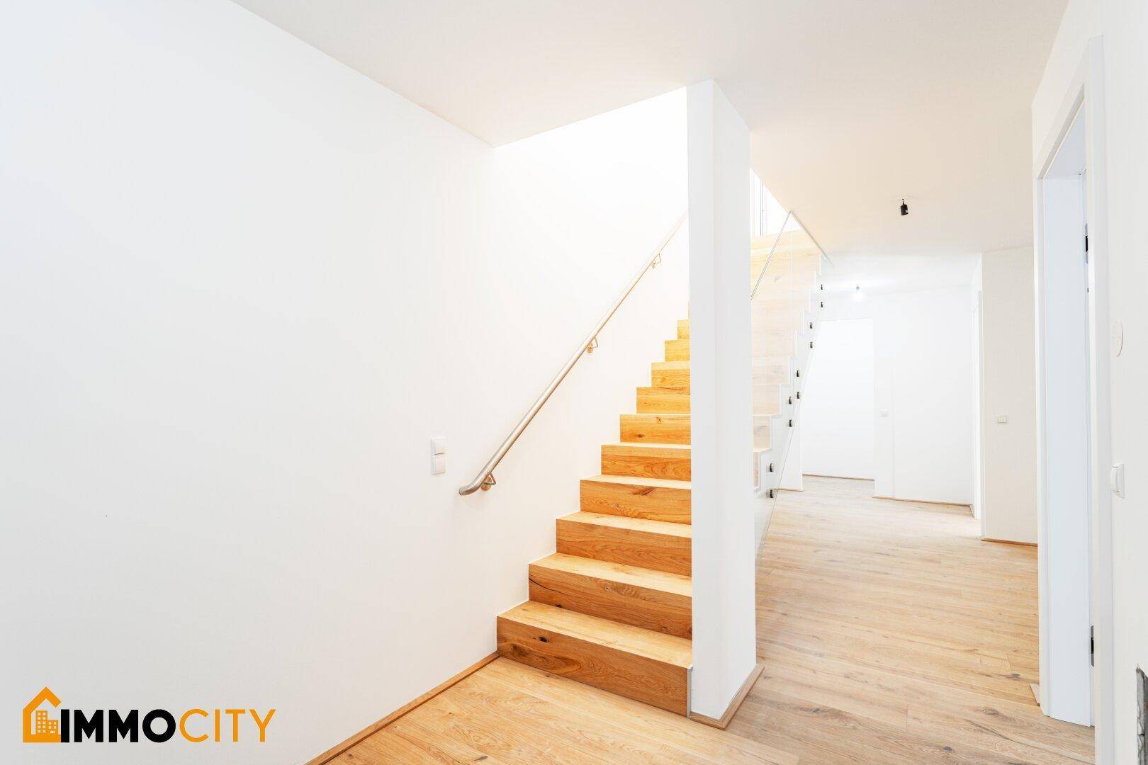 Heller Flur mit Holztreppe und Glasgeländer, führt zu den oberen Etagen der Wohnung.
