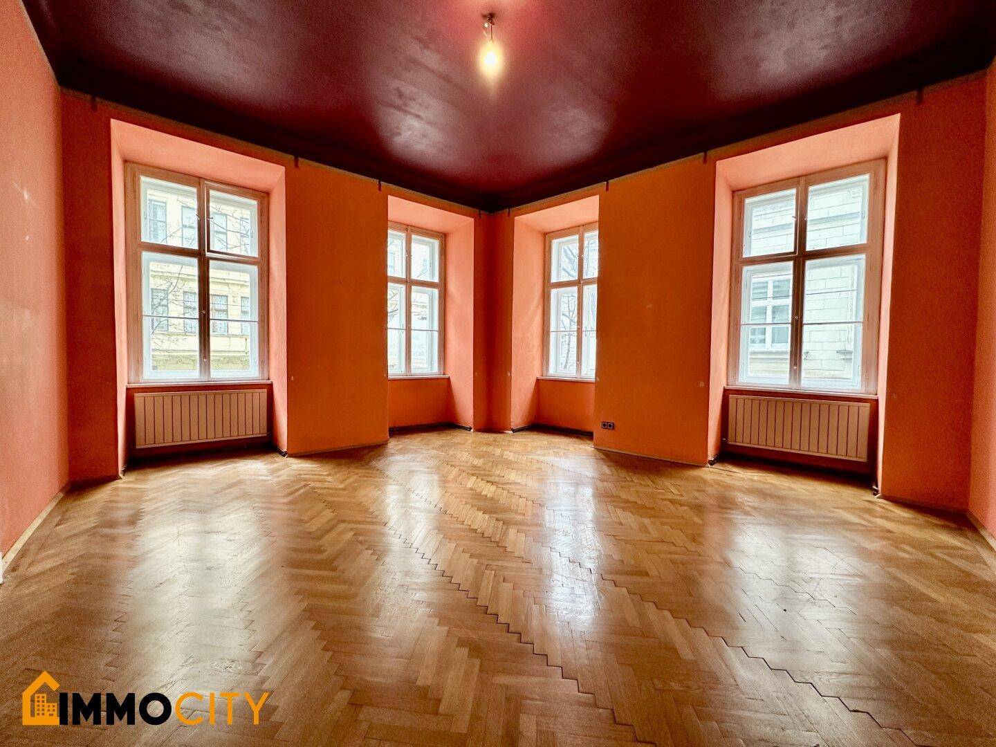 Geräumiges Zimmer mit Fischgrätparkett, hohen Fenstern und farbigen Wänden und Decke.