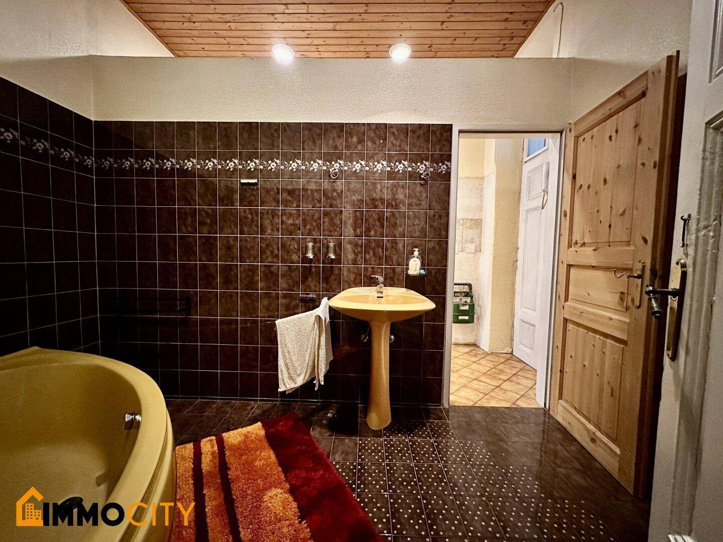 Badezimmer mit braunen Fliesen, Eckbadewanne und Holzdecke, im traditionellen Stil.