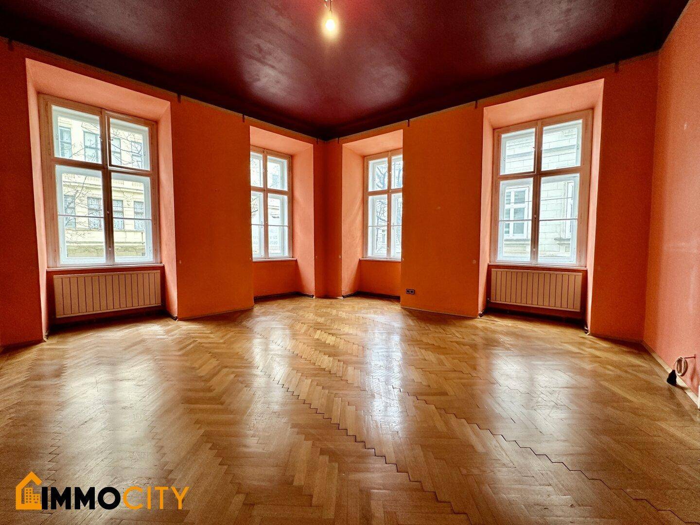 Geräumiges Zimmer mit Fischgrätparkett, hohen Fenstern und farbigen Wänden und Decke.